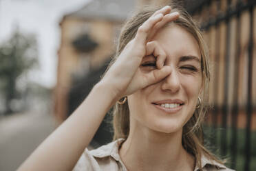 Smiling young woman winking eye gesturing OK sign - MFF08958