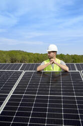 Engineer wearing hardhat between solar panels on roof - VEGF05531