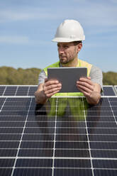 Ingenieur mit Schutzhelm und Tablet-PC zwischen Solarzellen auf dem Dach - VEGF05532