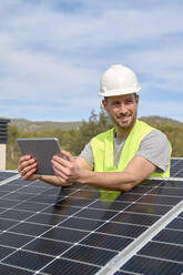 Lächelnder Ingenieur mit Tablet-PC zwischen Sonnenkollektoren auf dem Dach - VEGF05533