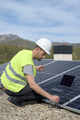 Ingenieur mit Laptop-Stromversorgungskabel vor Sonnenkollektoren an einem sonnigen Tag - VEGF05547