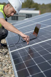Ingenieur, der an einem sonnigen Tag ein Ladegerät für ein Laptop-Netzteil an ein Solarmodul anschließt - VEGF05548