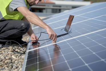 Ingenieur, der ein Laptop-Netzteilkabel-Ladegerät an die Solarzellen anschließt - VEGF05549