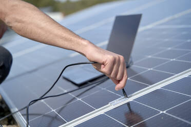 Ingenieur beim Einstecken des Stromversorgungskabels des Laptop-Ladegeräts in die Solarzellen - VEGF05550