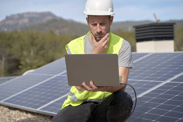 Ingenieur mit Hand am Kinn vor einem Laptop vor Sonnenkollektoren - VEGF05553