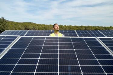 Engineer with eyes closed between solar panels on sunny day - VEGF05561