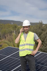Ingenieur, der mit einem Mobiltelefon spricht, während er an einem sonnigen Tag vor einem Solarpanel steht - VEGF05575