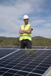 Lächelnder Ingenieur mit verschränkten Armen inmitten von Sonnenkollektoren - VEGF05576