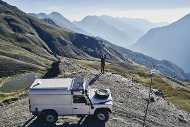 Woman with arms raised standing by off-road vehicle looking at view on sunny day - SSCF01081