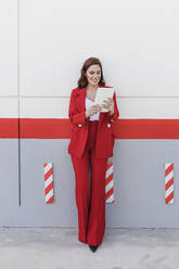 Smiling businesswoman with tablet PC standing in front of wall - JRVF02889