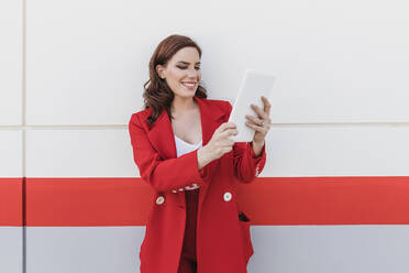 Happy businesswoman using tablet PC in front of wall - JRVF02890