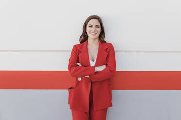 Smiling businesswoman with arms crossed leaning on wall - JRVF02895