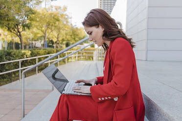 Freelancer using laptop on steps outdoors - JRVF02900