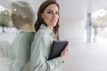 Businesswoman with diary leaning on glass window - JRVF02915