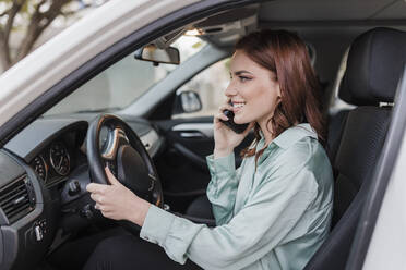 Lächelnde Geschäftsfrau, die im Auto sitzt und mit dem Handy telefoniert - JRVF02918