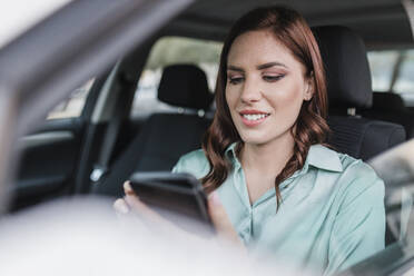 Lächelnde Geschäftsfrau mit Smartphone im Auto - JRVF02919