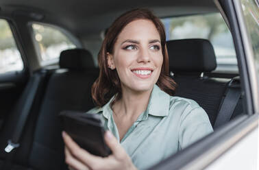Smiling businesswoman with smart phone sitting in car - JRVF02921