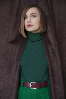 Beautiful woman in green turtleneck top standing amidst curtain - IYNF00100