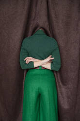 Frau mit hinter dem Rücken verschränkten Armen versteckt den Kopf in einem Vorhang - IYNF00103