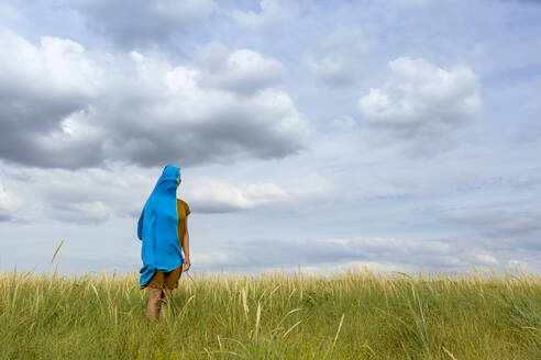Frau steht inmitten von Gras mit blauem Schal auf einer Wiese - OJF00498