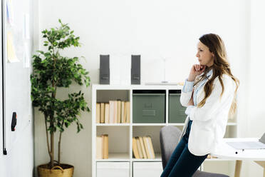 Thoughtful businesswoman with hand on chin looking at whiteboard in office - GIOF14956