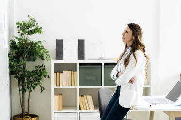 Businesswoman with arms crossed looking at whiteboard in office - GIOF14957