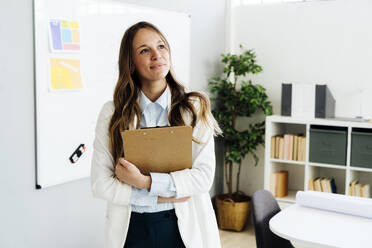 Businesswoman holding file folder standing in front of white board - GIOF15003