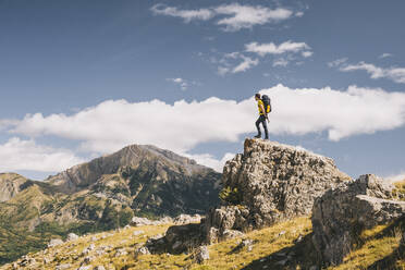 Young man summits small rock against the high mountains, Pyrenees - CAVF95977