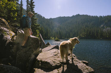 Guy and his dog standing next to an alpine lake - CAVF95981