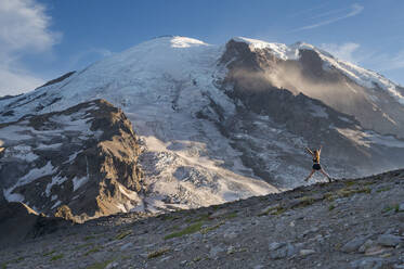 Fit female jumping with excitement on a ridge next to Mount Rainier - CAVF95982