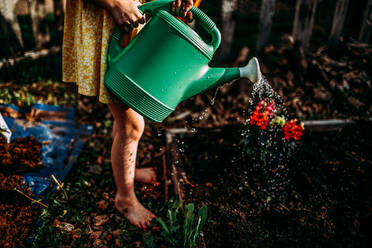 Junges Mädchen bewässert Blumen in einem Garten - CAVF95996