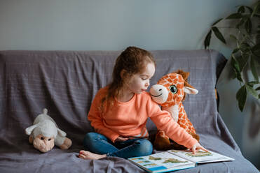 Kleinkind liest Spielzeug aus Büchern auf dem Sofa vor - CAVF96007