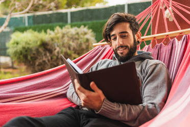 Entspannter Hipster-Mann in Hängematte beim Lesen der Agenda - CAVF96028