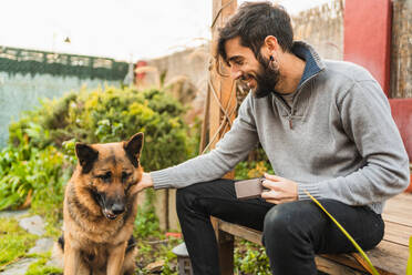 Lächelnder Mann beim Tee mit dem Hund im Garten - CAVF96029