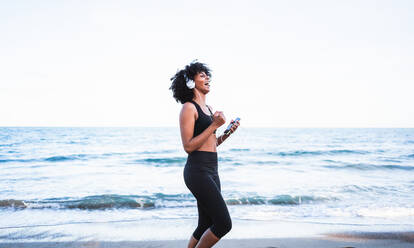 Black woman laughing and having fun listening to music on the beach - CAVF96034