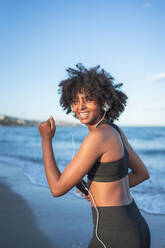 Schwarze Frau, die lacht und Spaß hat, während sie am Strand Musik hört - CAVF96038