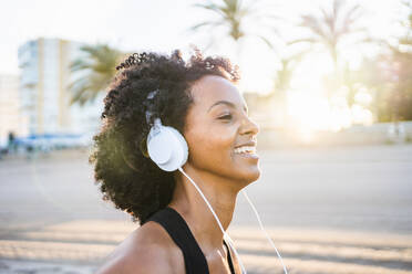 Black woman with afro hair dances listening to music on the beach - CAVF96042