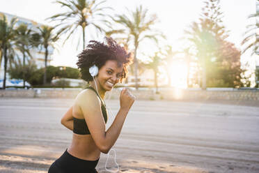 Schwarze Frau mit Afro-Haar läuft lächelnd am Strand - CAVF96045