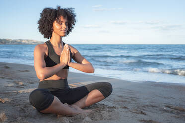 Black woman relaxed sitting on the beach practicing yoga - CAVF96046