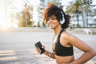 Black woman with afro hair runs listening to music at sunrise - CAVF96049