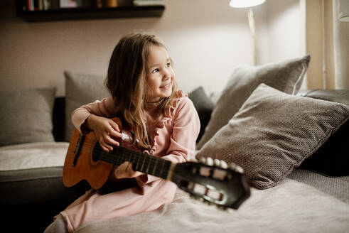 Beautiful smiling little girl playing the acoustic guitar at home. - CAVF96068