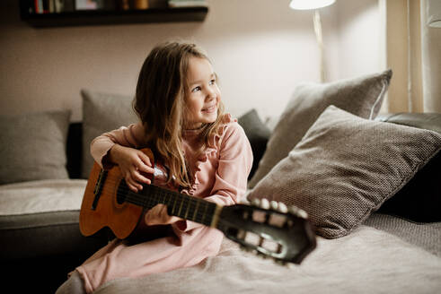 Schönes lächelndes kleines Mädchen, das zu Hause auf der Akustikgitarre spielt. - CAVF96068