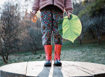 Kind steht im Wald mit Blättern in der Hand und spielt - CAVF96076