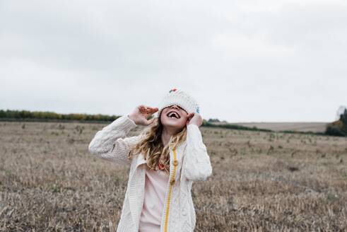 Lachendes Mädchen auf einem Feld, das mit einem Hut über den Augen spielt - CAVF96078