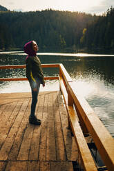 Woman standing near mountain lake at sunset - CAVF96092