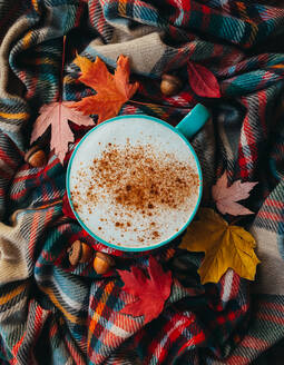 Overhead of pumpkin spice latte on plaid fall scarf with leaves - CAVF96136