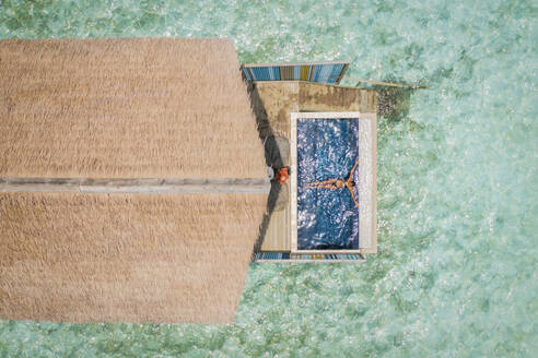 Aerial Top Down View Of Woman Relaxing In Luxury Resort Villa Swimming Pool Beside Clear Blue Ocean In Male, Maldives. - AAEF14268