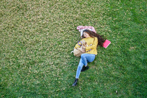 Top view full body of female owner with cute dog lying on green grassy lawn in park on summer day - ADSF34168