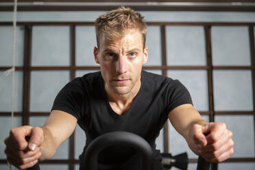 Serious male athlete in sportswear doing exercise on modern cycling machine during workout in gym and looking away - ADSF34172