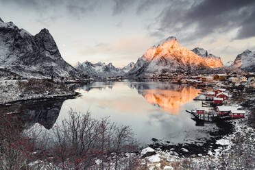 Wolken in der Morgendämmerung über dem traditionellen Rorbu und dem Berg Olstind, der sich im Meer spiegelt, Reine Bay, Nordland, Lofoten, Norwegen, Skandinavien, Europa - RHPLF21758